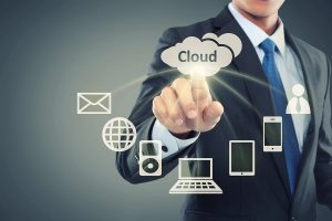 A businessman in a suit interacts with icons representing cloud computing and digital devices, including a cloud labeled "Cloud," email, a globe, and various electronic devices, against a gradient background.