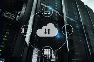 A server room with sleek black racks illuminated by green and blue lights, featuring a central cloud icon with upload and download arrows, surrounded by icons representing a desktop computer, a laptop, and a smartphone.